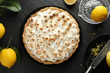 Delicious meringue pie, lemons, grater and squeezer on black textured table, flat lay