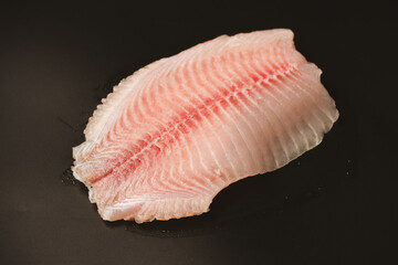 Fresh tilapia fillet on black background, top view.
