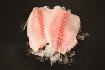 Fresh tilapia fillet on ice on black background