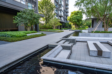 a stylish, landscaped pathway winding through a contemporary residential apartment complex, featuring a tiled walkway, a modern courtyard, accented by a water feature, and sleek stone seating