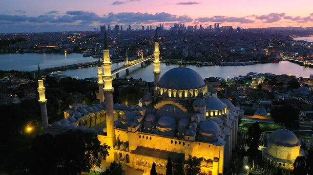 Magnificent S&uuml;leymaniye Mosque in Istanbul glows at sunset during Ramadan, with its minarets and domes highlighted against the Golden Horn, the Galata and Hali&ccedil; bridges visible in the serene backgroun