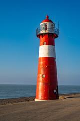 Fototapeta premium The red and white lighthouse Noorderhoofd at the Dutch coast near Westkapelle, Province of Zeeland, Netherland