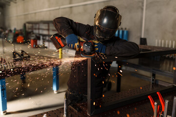 Metalworker wearing protective gear operates a grinder on a metal frame, creating a dazzling shower...