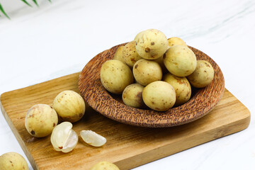 Duku fruits on a wooden plate with white marble background. One of Indonesian tropical fruit.