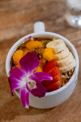 Fresh tropical fruit smoothie bowl with banana, mango, strawberries, and an orchid garnish