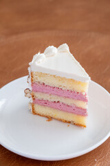 A slice of vanilla and raspberry layered cake with whipped frosting on a white plate
