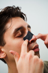 Young guy applying charcoal nose strip for deep nose pores cleaning. Male beauty and skincare...