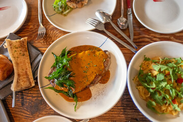 Rustic dinner setting with multiple gourmet dishes including a plated meat dish and fresh side salads