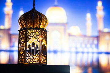 ornamental Arabic lantern with burning candle glowing at night and mosque in background. Festive...