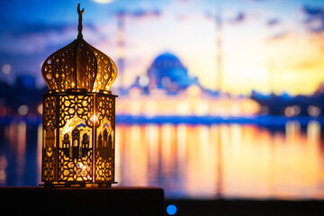 ornamental Arabic lantern with burning candle glowing at night and mosque in background. Festive...
