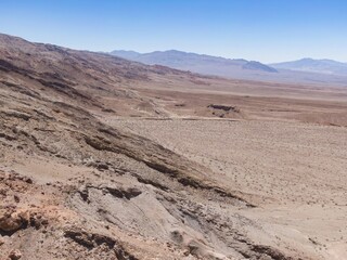 Arid landscape of Death Valley National Park, California, USA. The image shows the dry, rocky terrain and distant mountains under a clear blue sky.