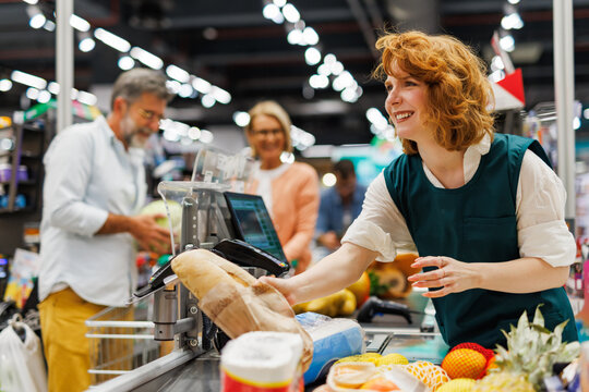 Smiling cashier scanning groceries at supermarket checkout