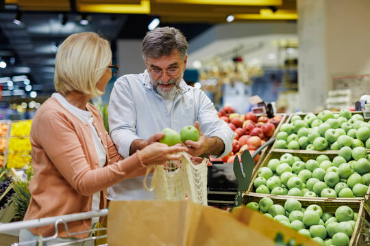 Senior couple choosing green apples in grocery store