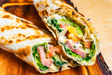 Tasty wrap with fresh veggies and meats on a wooden board