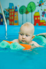Child learns to swim with coach in pool. Swimming in children's pool. Happy child with coach in indoor pool playing and having fun.