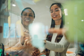 Smiling businesswomen planning strategy using sticky notes on glass wall