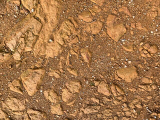 Close-up of a textured dry rocky soil surface with small stones, pebbles, and cracks in earthy brown tones. Natural ground and geology concept.