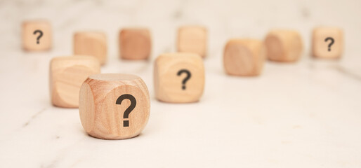 wooden blocks with question marks on a marble surface, symbolizing uncertainty and curiosity