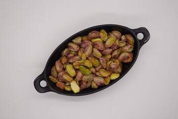 Roasted pistachios filling a black ceramic bowl on white background