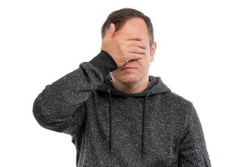A young man in a gray hoodie covering his face with one hand against a white background.