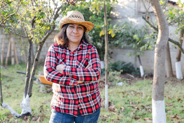 Senior Hispanic woman in her backyard - female farmer with arms crossed smiling at camera