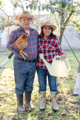 Happy senior couple on their farm carrying a chicken - Hispanic farmers with a chicken in their yard