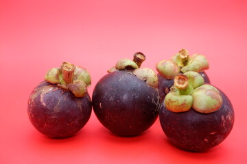 Isolated mangosteen fruit on a red surface, displaying its thick outer shell and fresh appearance.