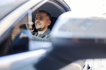 Young smiling man driving his car and talking on his phone.