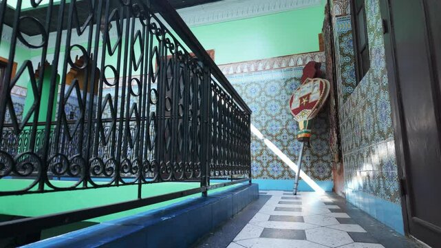 Moroccan-style balcony with intricate wrought iron railing, patterned tile walls and decorated musical instrument, illuminated by natural sunlight