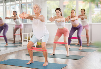 Obraz premium Group of women standing on mats and doing stretch exercises with resistance bands