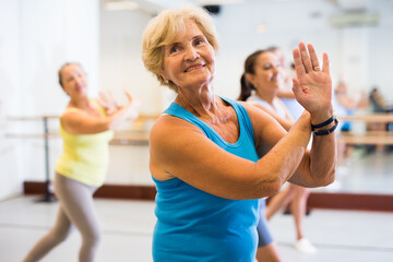 Portrait of an active mature European woman enjoying modern energetic dancing in a female group in the studio