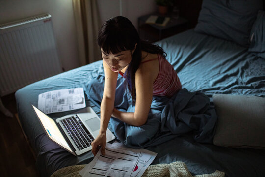 Asian woman doing financials in bed with laptop