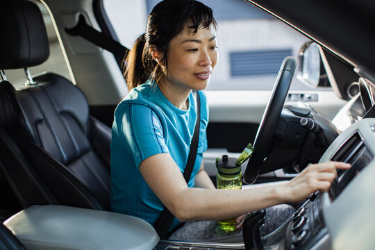 Woman in sportswear sitting in car drinking water after workout