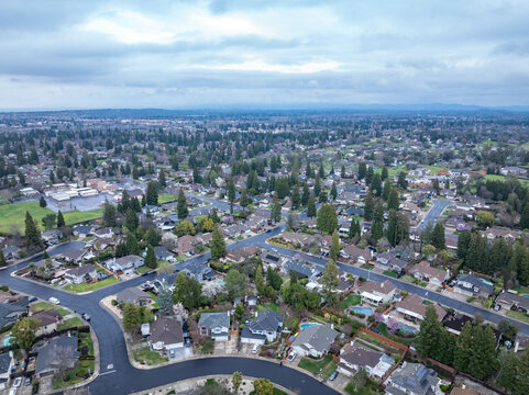 Aerial photographs over the Maidu Neighborhood in Roseville, California with green trees, streets, homes and a cloudy sky