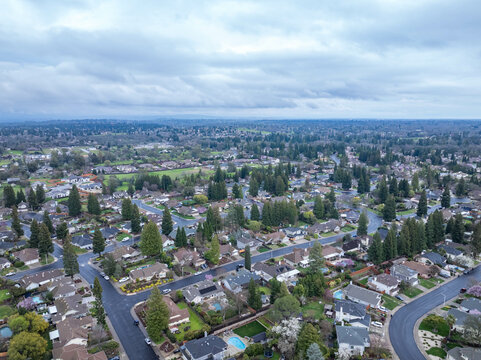 Aerial photographs over the Maidu Neighborhood in Roseville, California with green trees, streets, homes and a cloudy sky