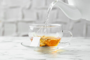 Pouring hot water into cup with tea bag on light marble table, closeup
