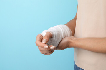 Woman with medical bandage on wrist against light blue background, closeup