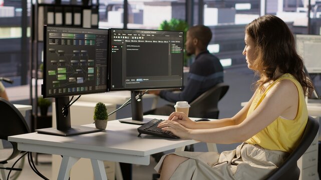 Manager in wheelchair passing by desk of employee testing machine learning company software to minimize occurrence of bugs. Woman works in inclusive workspace with workers with disabilities, camera A