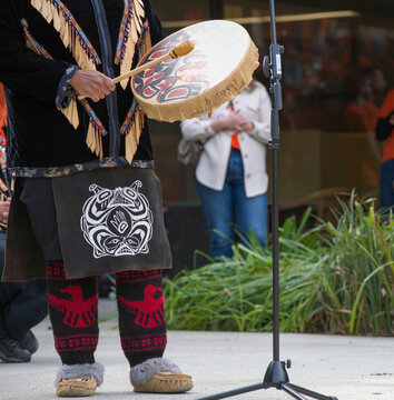 A dancer in regalia from the Squamish Nation in British Columbia, Canada performs with a drum.

