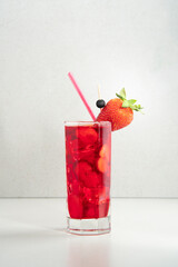 strawberry cocktail with ice in glass on ceramic table against grey background