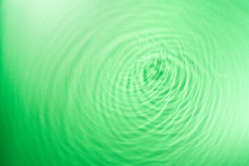 water droplet waves expanding on the water surface illuminated with green light