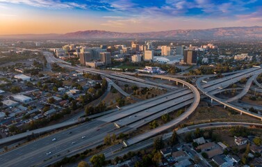 Aerial view of San Jose, California, USA, at sunset. Cars travel on the highway interchange, connecting the city's downtown with the surrounding areas. The mountains are in the background.