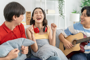 Diverse Asian friends playing guitar and dancing in living room at home.