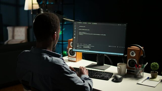 African american expert at desk using pc for programming and data analysis. Young networking expert working from his home setup, manages information technology and data center. Camera A.