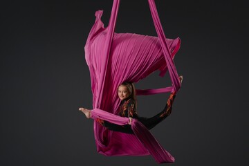 Girl performs aerial silk routine using vibrant pink fabric in a studio setting