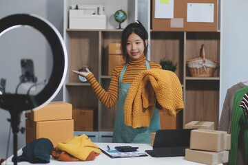 vlogger, blogger small SME business asian beautiful woman using mobile phone video call for sell clothes live stream selling online, show product present detail at home office, entrepreneur ecommerce