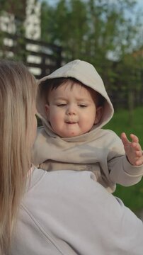 Mother holds one year old baby in her arms during a walk in the summer. Vertical video
