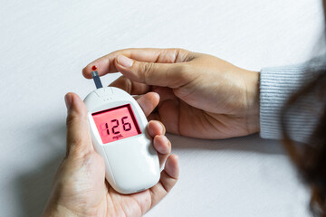 Woman's hands checking diabetes and hyperglycemia with digital blood sugar meter. Healthcare and...