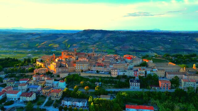 Splendid aerial push-in pedestal down shot from Montefiore dell'Aso (AP) with the town centre's buildings, roads, trees, reddish sunlight imbuing the churches and bell towers, hillscapes
