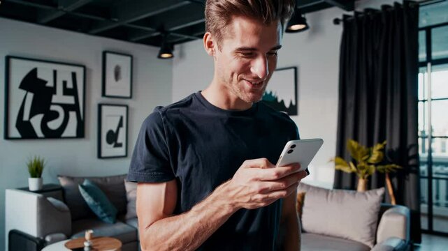 A man smiling at his phone in a modern living room, captured from a mid-angle. The video concept is casual and contemporary, with artistic decor.